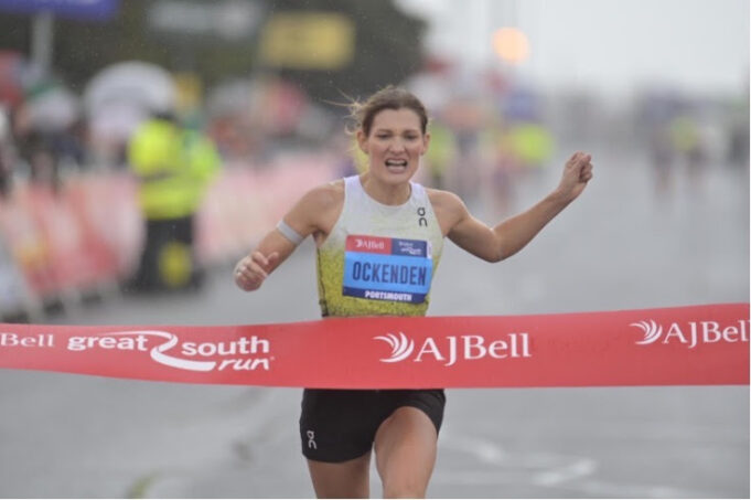 Great South Run Woman runs hard through red tape of a finish line