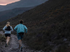 A man an woman run along a hilly trail in low light
