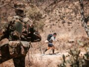 The ultramarathon running through the heart of conservation Image shows back of a ranger in the froeground as an ultra runner passes in front of him in the distance.