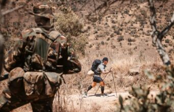 The ultramarathon running through the heart of conservation Image shows back of a ranger in the froeground as an ultra runner passes in front of him in the distance.