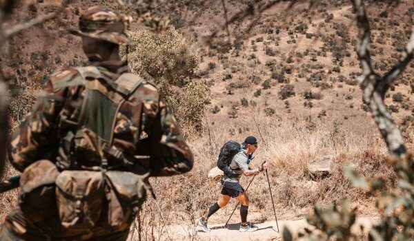 The ultramarathon running through the heart of conservation Image shows back of a ranger in the froeground as an ultra runner passes in front of him in the distance.