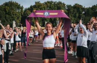 Esmée Gummer completes The Nation’s 5k A young woman holds a finish tape above her head. She looks emotional but happy. She is surrounded by people clapping