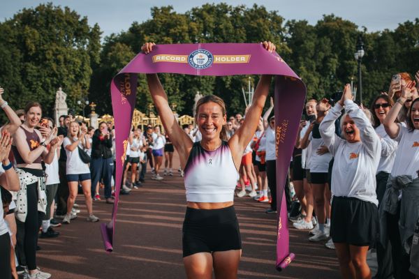 Esmee Gummer A young woman holds a finish tape above her head. She looks emotional but happy. She is surrounded by people clapping