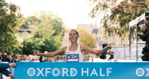 Woman runs through light blue finish tape saying Oxford Half