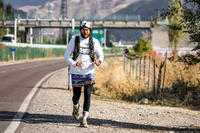 Man runs along side of a road with mountains in the background