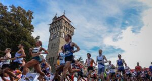 A crowd of road runners running fast past a tower