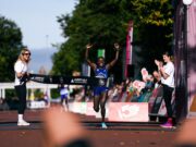 New women’s course record at Cardiff Half Woman runs through finish tape, her hands above her head, smiling.