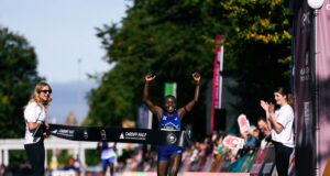 Woman runs through finish tape, her hands above her head, smiling.