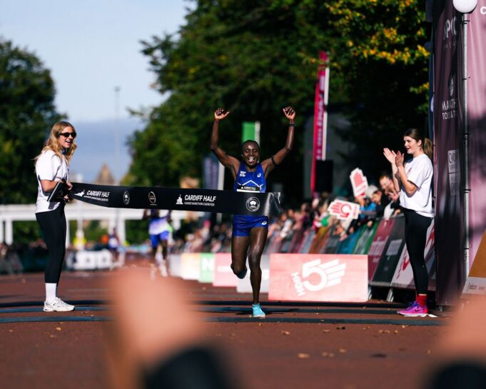 Cardiff Half Marathon Woman runs through finish tape, her hands above her head, smiling.