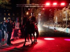 Kullamannen by UTMB® race week underway Knight in armour on a black horse walks over a finish line which is lined with spectators. It is night time and the finish area is carpeted in red.