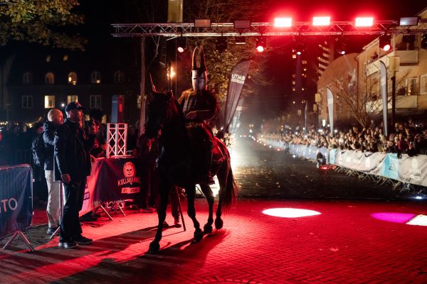 Kullamannen 2025 Knight in armour on a black horse walks over a finish line which is lined with spectators. It is night time and the finish area is carpeted in red.