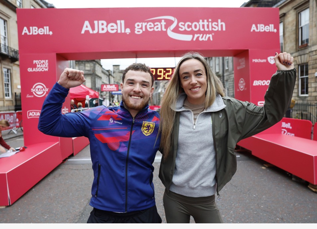 Great Scottish Run Eilish McColgan and a young man stand in front of the start line, arms around shoulders, one arm each in the air, smiling